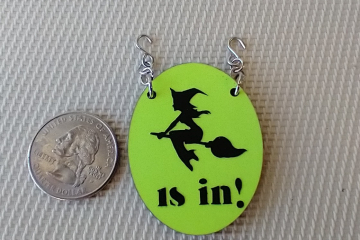 1:12 scale dollhouse Halloween oval sign featuring flying witch "is in" on bright yellow glow-in-the-dark background