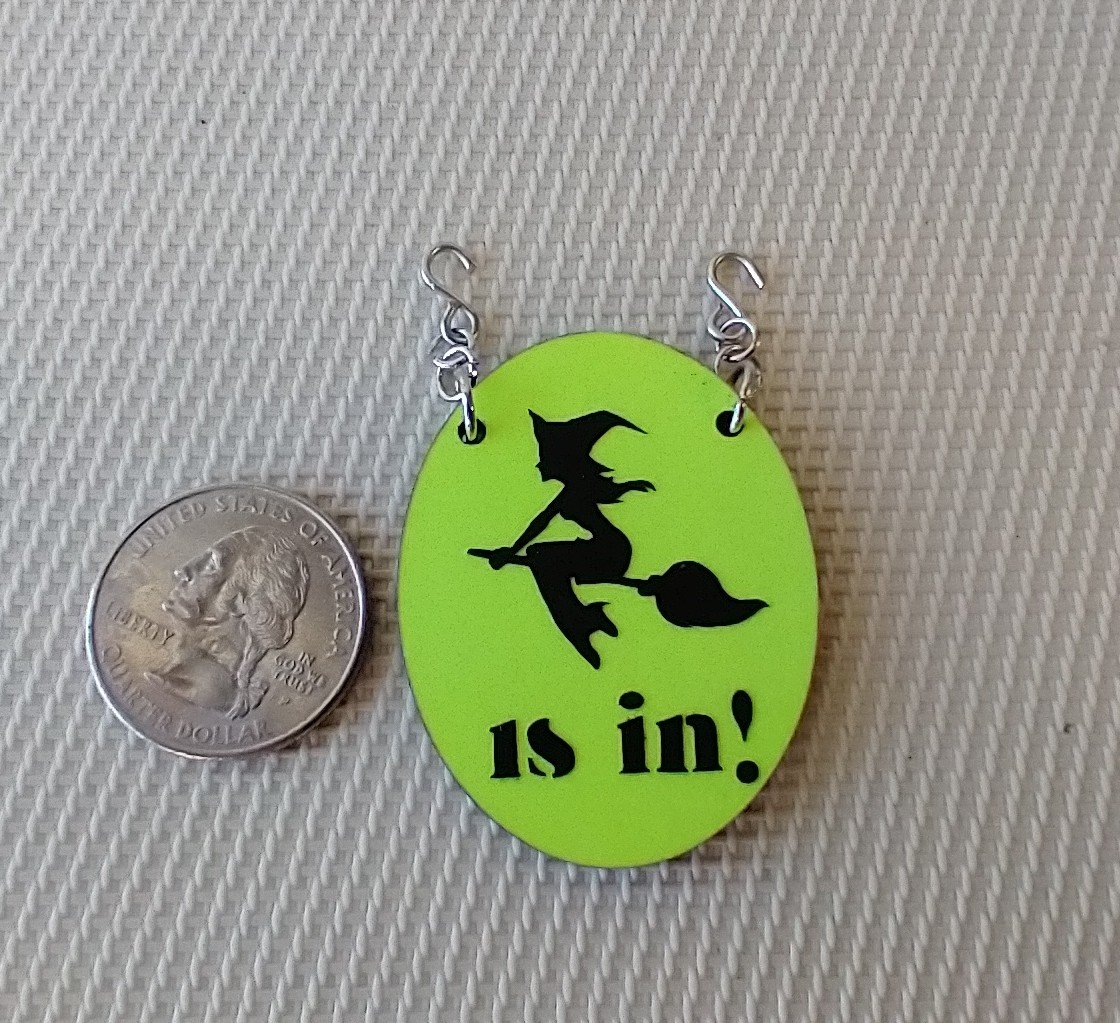 1:12 scale dollhouse Halloween oval sign featuring flying witch "is in" on bright yellow glow-in-the-dark background